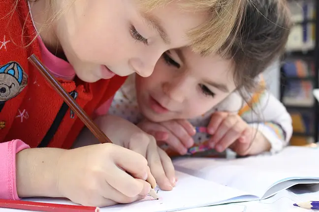 Zwei jüngere Kinder schreiben in einem Arbeitsheft.